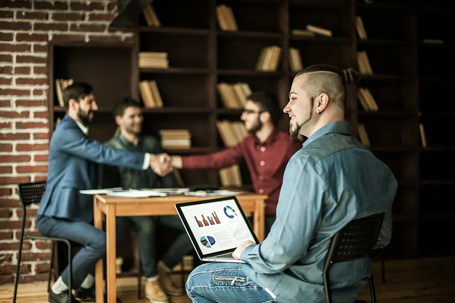 Business professionals discussing pitch deck templates in a meeting, with a presenter showing charts and graphs on a laptop screen.