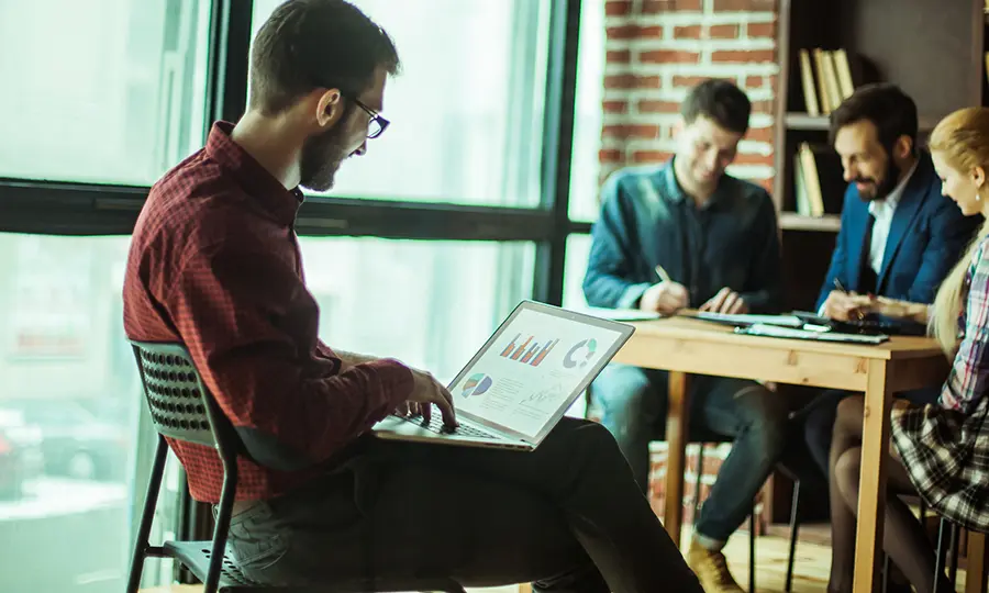 Team discussing an investor pitch deck with graphs and charts on a laptop, focusing on pitch deck tips and storytelling techniques.