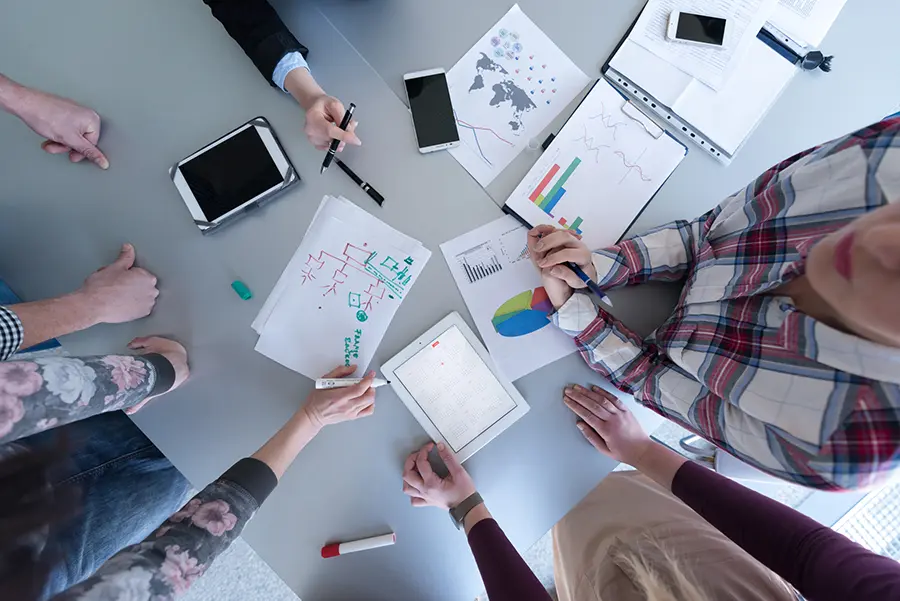 Aerial view of business people brainstorming during a meeting, illustrating the collaborative process of creating startup documents like pitch decks and business plans.