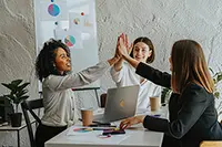 A team of three professionals celebrating successful presentation design using AI, in an office setting with visible graphs and laptops.