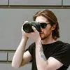 Profile photo of Alex Hahn, a man wearing sunglasses and holding a camera, taking a photo.