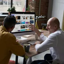 Two professionals collaborating on a computer screen displaying hicreo.com, the AI-powered presentation software, in a modern office setting.