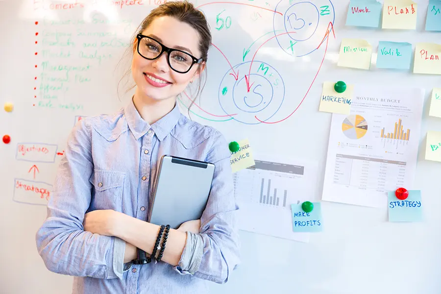 Smiling young woman using hicreo.com to create a compelling presentation on a whiteboard with graphs and charts.